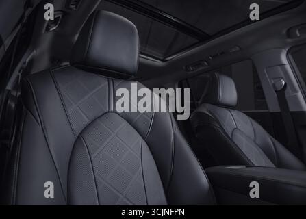 SUV-Innenraum mit Ledersitzreihen bei Nacht. Vordere Reihe von Autositzen im Fokus und dunkler Innenraum im Hintergrund. Stockfoto