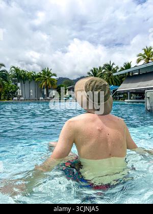 Ein Mann, der sich in einem Pool sonnt. Ein gesichtsloser Kerl mit Hut in einem Außenpool Stockfoto