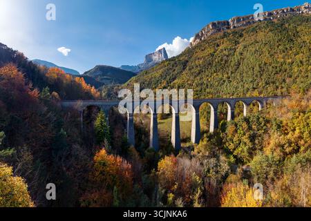 Herbstansicht eines Eisenbahnviadukts in der Region Trieves, Isere, Frankreich. Alpenlandschaft mit farbenfrohen Wäldern, Mont Aiguille und dem Vercors-Massiv Stockfoto