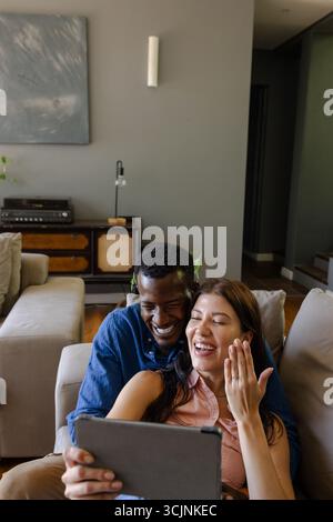 Paare lachen, während Videochats auf einem Tablet zu Hause und genießen die Zeit in guter Qualität Stockfoto