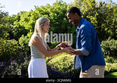 Feiert die Verlobung, ein Paar, das Lächeln und Lachen im sonnigen Garten tauscht Stockfoto