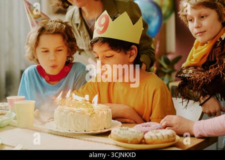 Kaukasische Jungs und Mädchen feiern Geburtstag und blasen Kerzen auf Kuchen aus Stockfoto