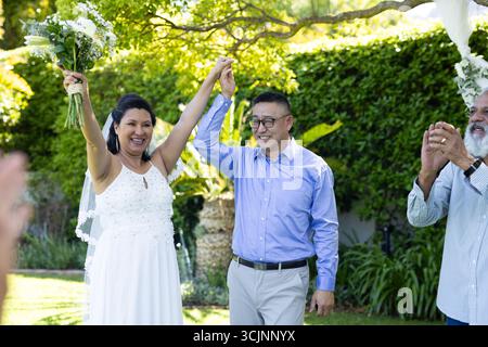Die Hochzeit der Senioren im Freien, das fröhliche Paar hält die Hände und lächelt mit den Gästen Stockfoto