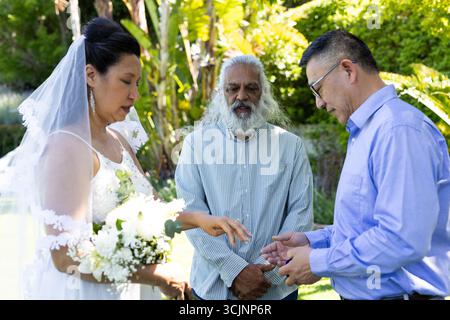 Austausch von Ringen, Braut und Bräutigam mit dem Offiziellen während einer Hochzeitszeremonie im Freien Stockfoto