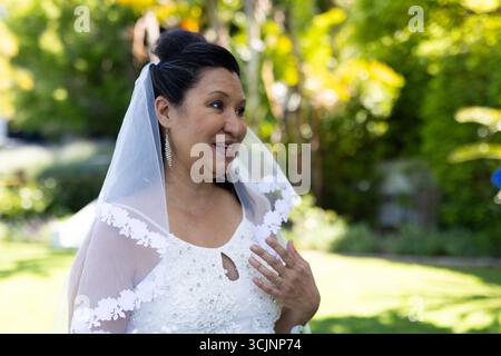 Im Garten lächelt Braut in weißem Kleid, umgeben von wunderschönen Blumen Stockfoto