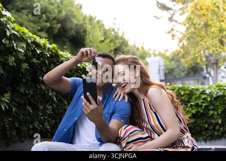 Ein junges Paar lächelt und hält Schlüssel, während es draußen Selfie macht Stockfoto