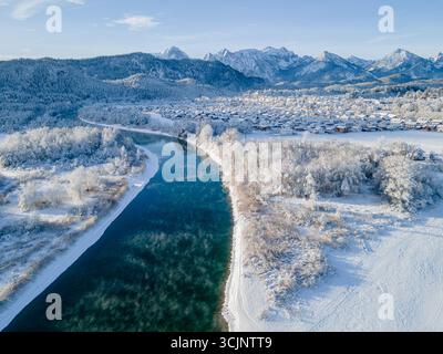 Aus der Vogelperspektive eines ruhigen Flusses, der durch eine schneebedeckte Landschaft in der Nähe der fernen Berge in Füssen, Bayern, Deutschland schneidet. Stockfoto
