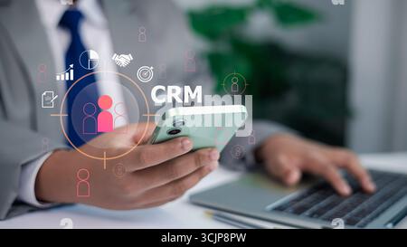 Geschäftsmann, der ein Smartphone mit digitalen CRM-Symbolen hält, symbolisiert Kundenbeziehungsmanagement, Vertrieb, Marketing, Analysen und Technologie Stockfoto