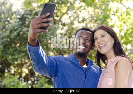 Ein Paar macht Selfie im Freien, lächelt und genießt einen sonnigen Tag im Park Stockfoto