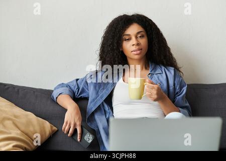 Afroamerikanerin entspannt sich während der Arbeit von zu Hause aus und genießt eine Tasse Tee in ihrer schicken Wohnung. Stockfoto