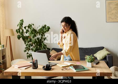 Eine schöne junge Frau arbeitet fernab und lächelt während eines Anrufs. Stockfoto