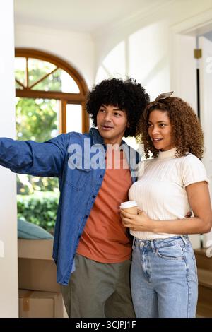 Junge, vielfältige Paare, die Kisten in einem neuen Zuhause auspacken, lächeln und den Moment genießen Stockfoto