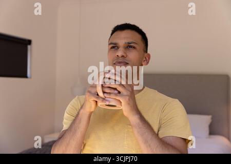 Junger Mann, der morgens Kaffee zu Hause genießt, nachdenklich und entspannt aussieht Stockfoto