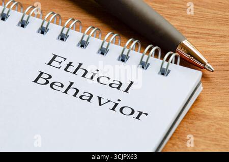 Schließen Sie den Notizblock mit den Worten ethisches Verhalten auf einer Seite, die auf einem Holzschreibtisch mit einem Bleistift daneben steht Stockfoto