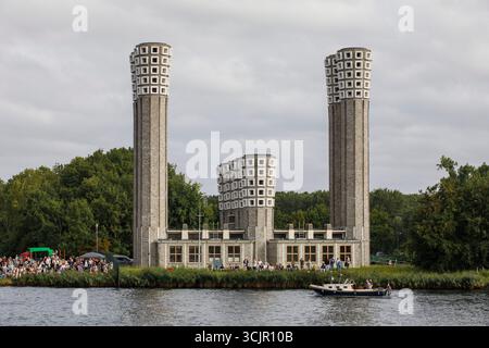 Segel-in-Parade des Sail Amsterdam, 20. August 2025, passiert ein kleines Boot die Lüftungstürme des Velser-Tunnels, Niederlande. Die Segel Amsterda Stockfoto