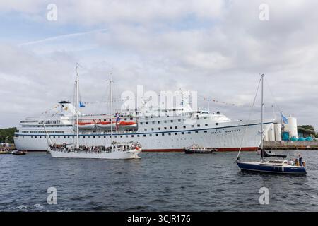 Segel-in-Parade der Sail Amsterdam, 20. August 2025, passiert ein zwei-Meister das ehemalige Kreuzfahrtschiff Ocean Majesty, das heute als Flüchtlingsunterkunft genutzt wird, ne Stockfoto