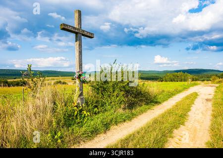 Altes christliches Kreuz auf der Landstraße in Ackerland am sonnigen Sommertag, Roztocze Nationalpark, Polen Stockfoto