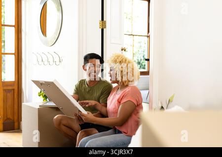 Junges, vielfältiges Paar, das zusammen auspackt und lacht, in einem neuen Zuhause, genießt Momente Stockfoto