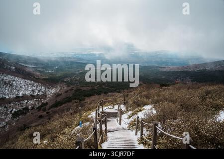 Schneebedeckte Holztreppen führen unter stimmungsvollen Wolken auf dem Yeongsil Trail, Hallasan, Jeju Island, Südkorea, hinab in eine riesige Waldlandschaft. Stockfoto
