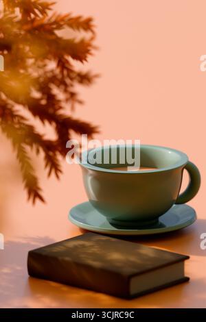 Eine Teetasse auf einer Untertasse neben einem Buch mit Herbstblättern, die eine gemütliche Herbstatmosphäre weckt. 3D-Rendering Stockfoto
