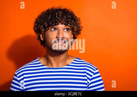 Porträt eines jungen Mannes mit lockigen Haaren, der ein gestreiftes Hemd vor einem leuchtend orangefarbenen Hintergrund trägt Stockfoto