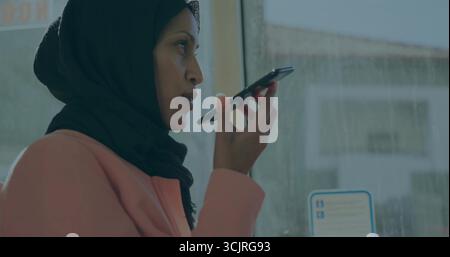 Telefon halten, das im Bus spricht, am nassen Fenster mit Aufkleber, Kopftuch und Mantel tragen, Kopierraum Stockfoto