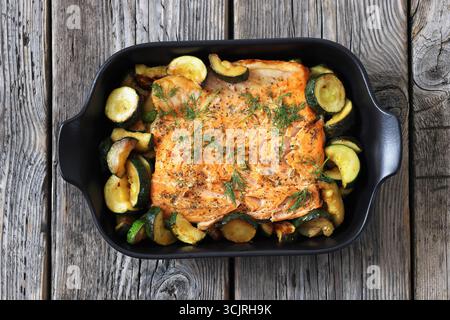 Gebacken im Ofen Lachsfilet mit Zucchini und Dill in schwarzer Auflaufform auf rustikalem Holztisch, Draufsicht, flache Lage, nicht AI generiert Stockfoto