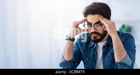 Überarbeitungs- und Terminkonzept. Gestresster arabischer Geschäftsmann, der Probleme bei der Arbeit hat, am Arbeitsplatz mit Laptop sitzt Stockfoto