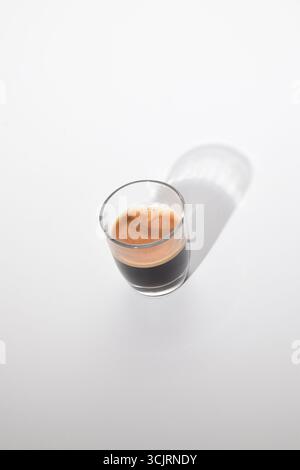 Minimalistisches Foto von Espresso-Kaffee in einer klaren Glasschale mit langem Schatten auf weißem Hintergrund, modernes Kaffeefotografiekonzept Stockfoto