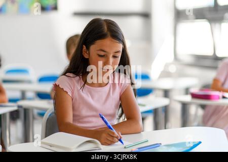 Fokussiertes Schulmädchen schreibt Notizen im Klassenzimmer. Stockfoto