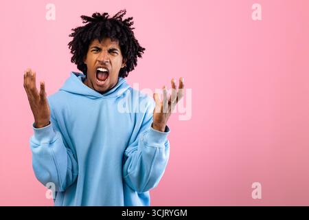 Wütender schwarzer Teenager, der vor Wut auf rosafarbenem Studiohintergrund schreit Stockfoto