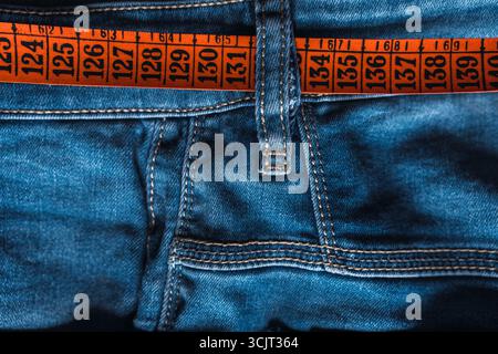 Vorderseite einer blauen Jeans mit offenem Knopf und gelbem und orangefarbenem Maßband. Stockfoto