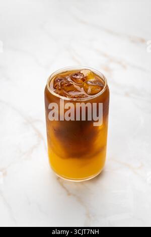 Erfrischender Eiskaffee mit Orangensaft in einem transparenten Glas auf Marmortisch Stockfoto