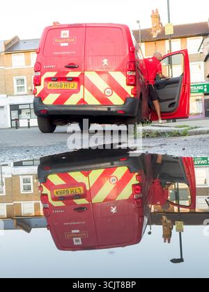 Royal Mail Delivery Driver verlässt den Van auf der Londoner Wohnstraße mit Reflections in Rainwater Puddle Stockfoto