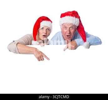 Seniorenpaar in Santa-Hüten zeigen auf ein weißes Poster Stockfoto