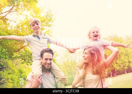 Kinder sitzen auf den Schultern ihrer Eltern in einem Park Stockfoto