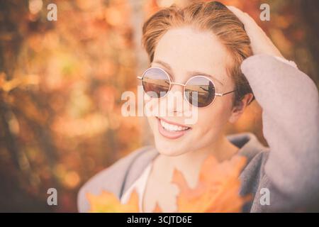 Rothaarige Frau mit Sonnenbrille im Herbstlaub, Porträt Stockfoto