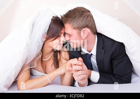 Frisch vermähltes Paar, das verliebt unter einer Decke liegt Stockfoto