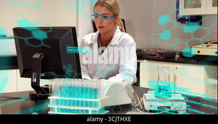 Forscher in weißer Beschichtung und Brille, die Daten auf Monitor im Labor überprüft, mit Reagenzglasgestell Stockfoto