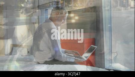 Sitzender reifer Mann, der am Laptop am Fenster in der Schlafzimmersuite arbeitet, mit Business-Hemd Stockfoto