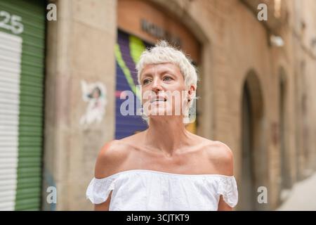 Eine Frau in einem weißen Kleid steht vor einem Gebäude. Sie hat einen ernsthaften Ausdruck im Gesicht Stockfoto
