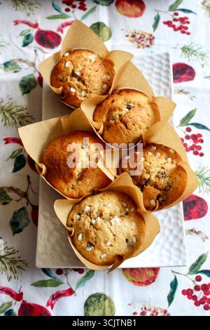 Teller mit frisch gebackenen Bananenmuffins, einige mit Zuckerhagelbelag, gegen ein Leinentuch mit Granatäpfeln, Blättern und Beeren. Stockfoto