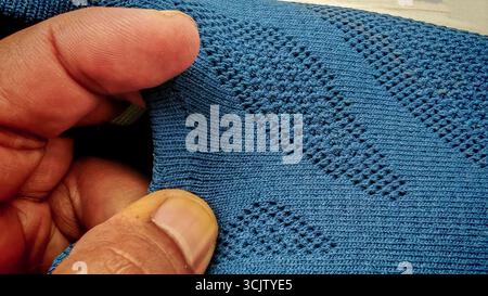 Strukturiertes blau-graues Gewebe aus gewebtem Mesh, das von den Händen gehalten wird und ein detailliertes Rautenmuster auf einem modernen Schuhmaterial hervorhebt. Stockfoto