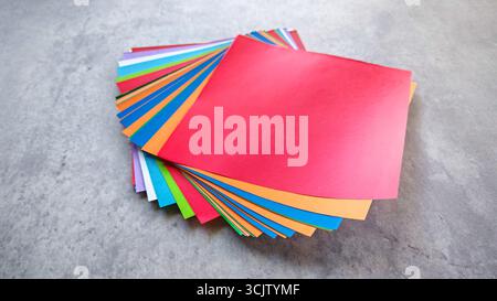 Ansicht von oben nach unten eines Stapels aus mehrfarbigem Origami-Papier auf einem grauen Stein- oder Betonhintergrund. Stockfoto