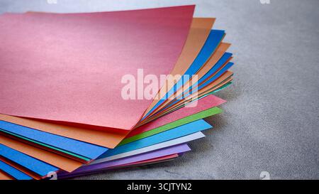 Ansicht von oben nach unten eines Stapels aus mehrfarbigem Origami-Papier auf einem grauen Stein- oder Betonhintergrund. Stockfoto