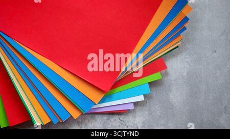 Ansicht von oben nach unten eines Stapels aus mehrfarbigem Origami-Papier auf einem grauen Stein- oder Betonhintergrund. Stockfoto