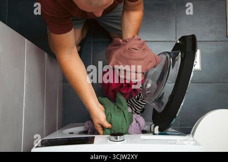 Blick von oben auf einen Mann, der schmutzige Kleidung in die Waschmaschine legte. Stockfoto