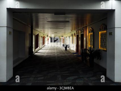 Blick auf einen langen Hotelkorridor mit dunklem Teppich und einzigartigen dekorativen Beleuchtungselementen, die eine stimmungsvolle Perspektive für den Innenraum schaffen Stockfoto