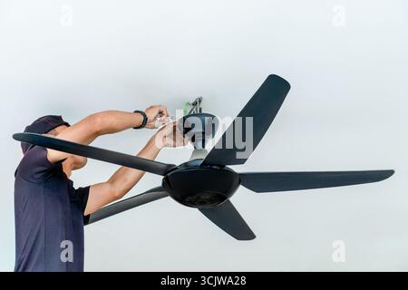 Ein Mann, der einen Deckenventilator installiert. Heimverbesserung, professionelle Arbeit und technisches Kompetenzkonzept. Stockfoto