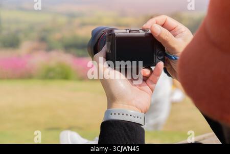 Mann, der Fotos mit einer Kamera macht, Erinnerungen festnimmt und einen Blick auf ein Bergblumenfeld wirft. Reisen, Touristen fotografieren Konzept. Stockfoto